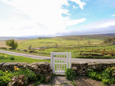 A white gate in a stone wall with a road and green fields in the background at Swinhope View in Hexham