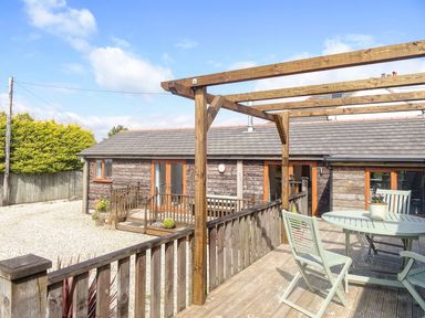 An outdoor wooden deck with a table and chairs and a pergola next to a wooden building at Lilys Pad in Okehampton