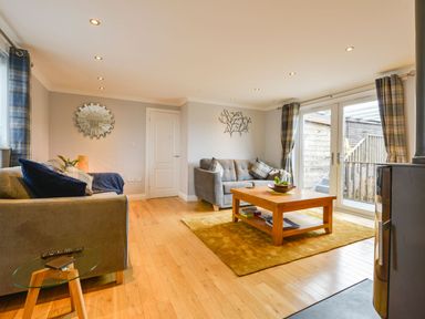A living room with two sofas a wooden coffee table a yellow rug and glass doors at Lilys Pad in Okehampton