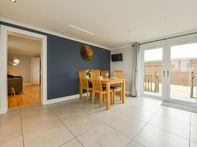 A dining area with wooden table and six chairs next to glass doors at Lilys Pad in Okehampton