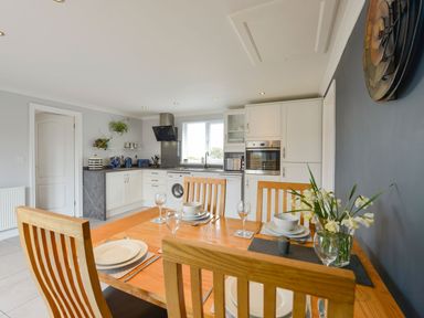 A kitchen and dining area with a wooden table set with plates glasses and flowers at Lilys Pad in Okehampton