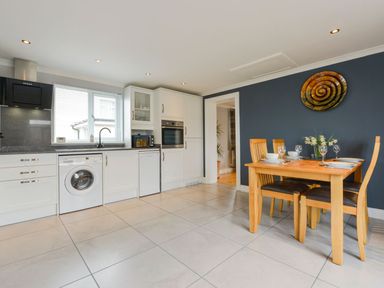 A kitchen with white cabinets appliances wooden dining table and chairs set for four at Lilys Pad in Okehampton