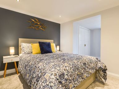 A bedroom with a bed with floral bedding and pillows next to a nightstand with a lamp at Lilys Pad in Okehampton