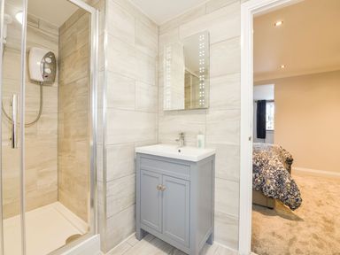 A bathroom with shower enclosure and sink cabinet next to a doorway leading to a bedroom at Lilys Pad in Okehampton