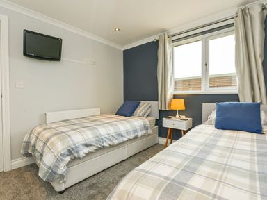 A bedroom with two single beds a nightstand with a lamp a window and a wall mounted television at Lilys Pad in Okehampton