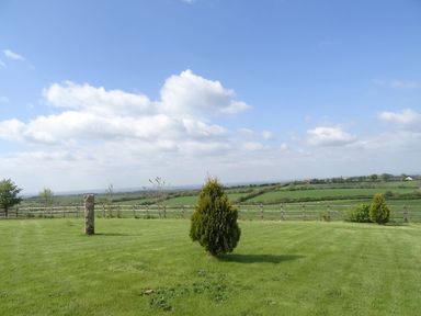 A grassy yard with small trees and a wooden fence overlooking fields at Lilys Pad in Okehampton