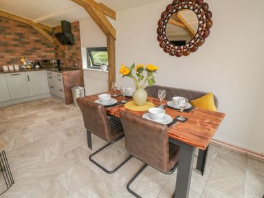 A dining area with a wooden table set for four people and a kitchen area with cabinets and utensils at Windy Willows in Okehampton