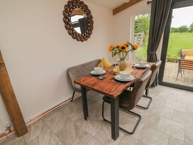 A dining area with a wooden table set for four with dishes and sunflowers by a glass door with a view of a garden at Windy Willows Okehampton