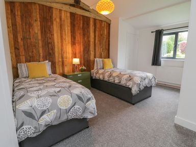 A bedroom with two single beds a wooden paneled wall and a window at Windy Willows in Okehampton