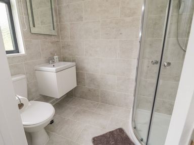A bathroom with a toilet sink mirror and curved glass shower at Windy Willows in Okehampton