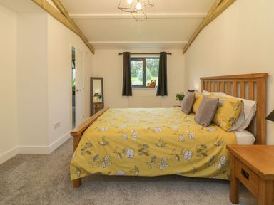 A bedroom with a wooden bed with yellow floral bedding a window with dark curtains and a wooden bedside table at Windy Willows in Okehampton