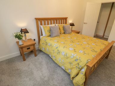 A bedroom with a wooden bed frame and yellow floral bedding with two bedside tables at Windy Willows in Okehampton