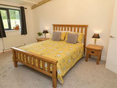 A bedroom with a wooden bed with yellow bedding and two bedside tables with lamps and a window with curtains at Windy Willows in Okehampton