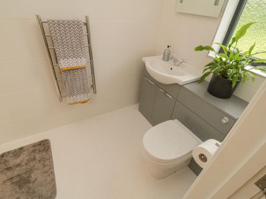 A bathroom with a toilet sink with gray cabinets a towel on a metal rack and a plant on the counter at Windy Willows in Okehampton