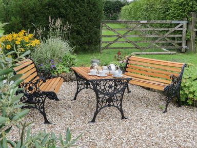 A garden seating area with two wooden benches and a table with tea set on gravel at Windy Willows in Okehampton