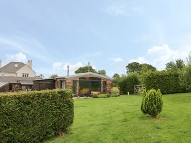 A garden with green grass bushes and a wooden house with large glass doors at Windy Willows in Okehampton