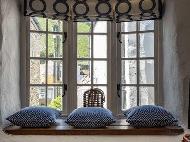 A window with three blue patterned cushions on the wooden sill and a wicker lantern in the middle at Sea Horses Port Isaac