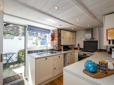 A kitchen with white cabinets a sink and countertop leading to an outdoor patio with table and chairs at Sea Horses in Port Isaac