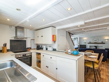 A kitchen with white cabinets and black countertop appliances next to a dining area with a wooden table and chairs at Sea Horses in Port Isaac