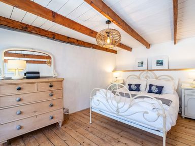 A bedroom with a metal bed frame two bedside tables and a wooden chest of drawers with a mirror at Sea Horses in Port Isaac