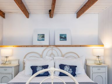 A bedroom with a bed two bedside tables and lamps wooden ceiling beams and two framed pictures on the wall at Sea Horses in Port Isaac