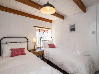 A bedroom with two single beds a wooden bedside table and a window at Sea Horses in Port Isaac