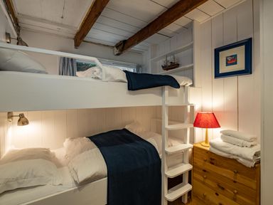 A bedroom with bunk beds blue blankets a wooden chest of drawers with folded towels and a red lamp at Sea Horses in Port Isaac