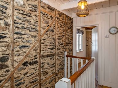 A hallway with a wooden railing stone and wooden wall and a light fixture at Sea Horses in Port Isaac