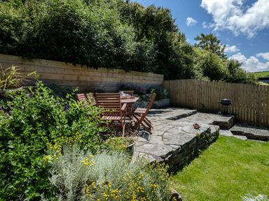 A garden patio with wooden chairs and table stone paving a charcoal grill and green plants at Sea Horses in Port Isaac