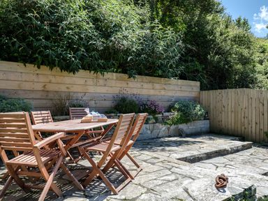 An outdoor patio area with a wooden table and chairs surrounded by plants and a wooden fence at Sea Horses in Port Isaac