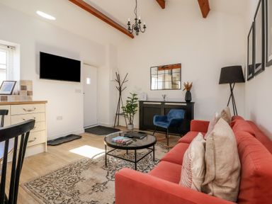 A living room with a red sofa a black round coffee table a blue chair and a wall mounted tv at Guillemot in Flamborough