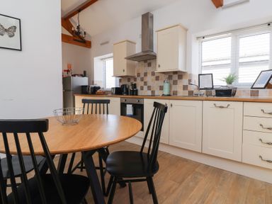 A kitchen with a round wooden table and black chairs with cream cabinets and a window at Guillemot in Flamborough