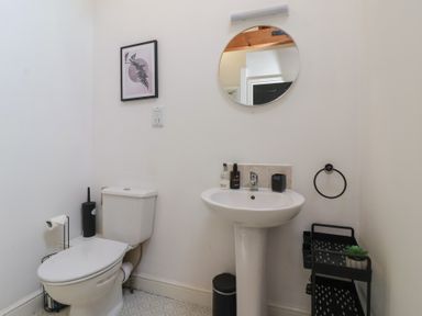 A bathroom with a toilet sink round mirror and a storage rack at Guillemot in Flamborough