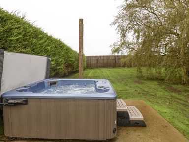 An outdoor hot tub on a concrete slab next to green grass with a wooden fence and hedges in the background at The Pheasantry in Flamborough