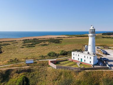 A lighthouse near the ocean with a grassy area and parking lot at The Pheasantry in Flamborough