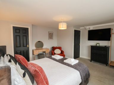 A bedroom with a bed, towels, mirror, chair, tv, and dresser at The Pheasantry in Flamborough