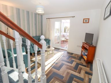 A living room with teal armchairs a small round table a television on a wooden stand and a sliding glass door leading to a sunroom at Hillside Hideaway in Wigton
