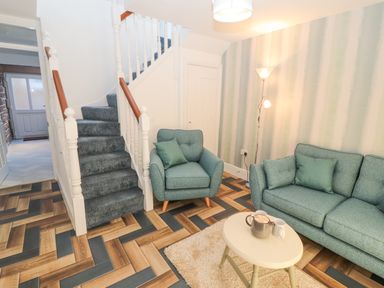 A living room with an armchair and sofa near stairs and a small round table at Hillside Hideaway in Wigton