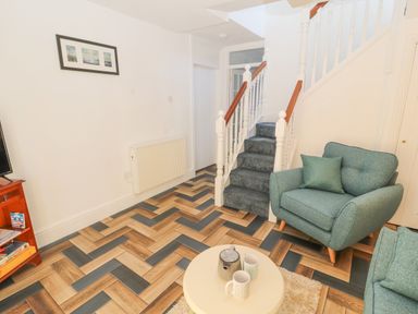 A sitting area with a green armchair and a round table with mugs in a room with stairs and patterned floor at Hillside Hideaway in Wigton