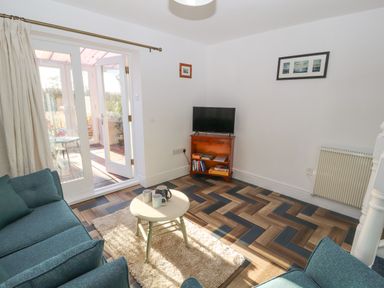 A living room with blue sofas small round table on a rug TV on wooden stand and glass doors leading to a sunroom at Hillside Hideaway in Wigton