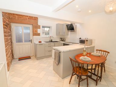 A kitchen with cabinets a sink microwave and a small round dining table with two chairs at Hillside Hideaway in Wigton