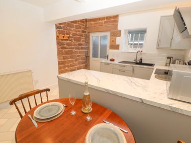 A kitchen with a wooden dining table set for two and a marble countertop at Hillside Hideaway in Wigton