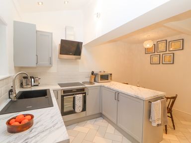 A kitchen with grey cabinets a black sink a built in oven a microwave and a dining area with wooden chairs at Hillside Hideaway in Wigton