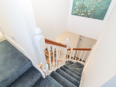 A staircase with blue carpet and white wooden banisters with brown handrails in a home at Hillside Hideaway in Wigton