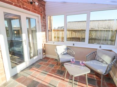 A sunroom with two chairs and a small table with two glasses on it at Hillside Hideaway in Wigton