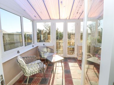 A sunroom with two chairs and a small table with glasses on it at Hillside Hideaway in Wigton