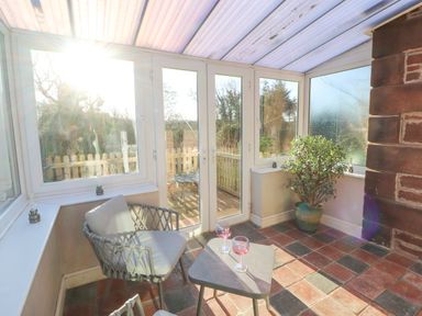 A sunroom with two chairs a small table with two glasses and a potted plant at Hillside Hideaway in Wigton