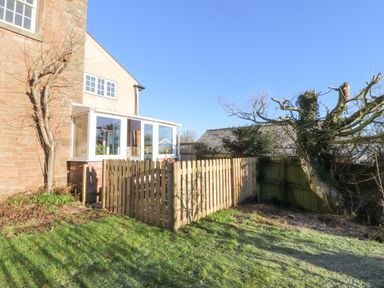 A garden area with a wooden fence next to a brick house and trees at Hillside Hideaway in Wigton