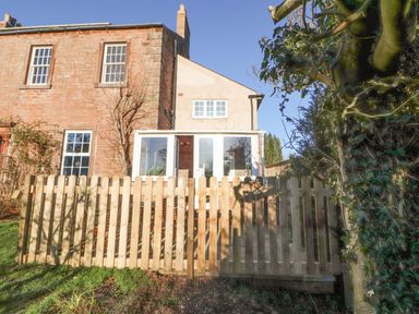 A garden with a wooden fence and a house with large windows at Hillside Hideaway in Wigton