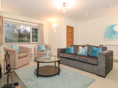 A living room with a gray sofa and two beige armchairs around a glass coffee table at Tandarra in Keswick